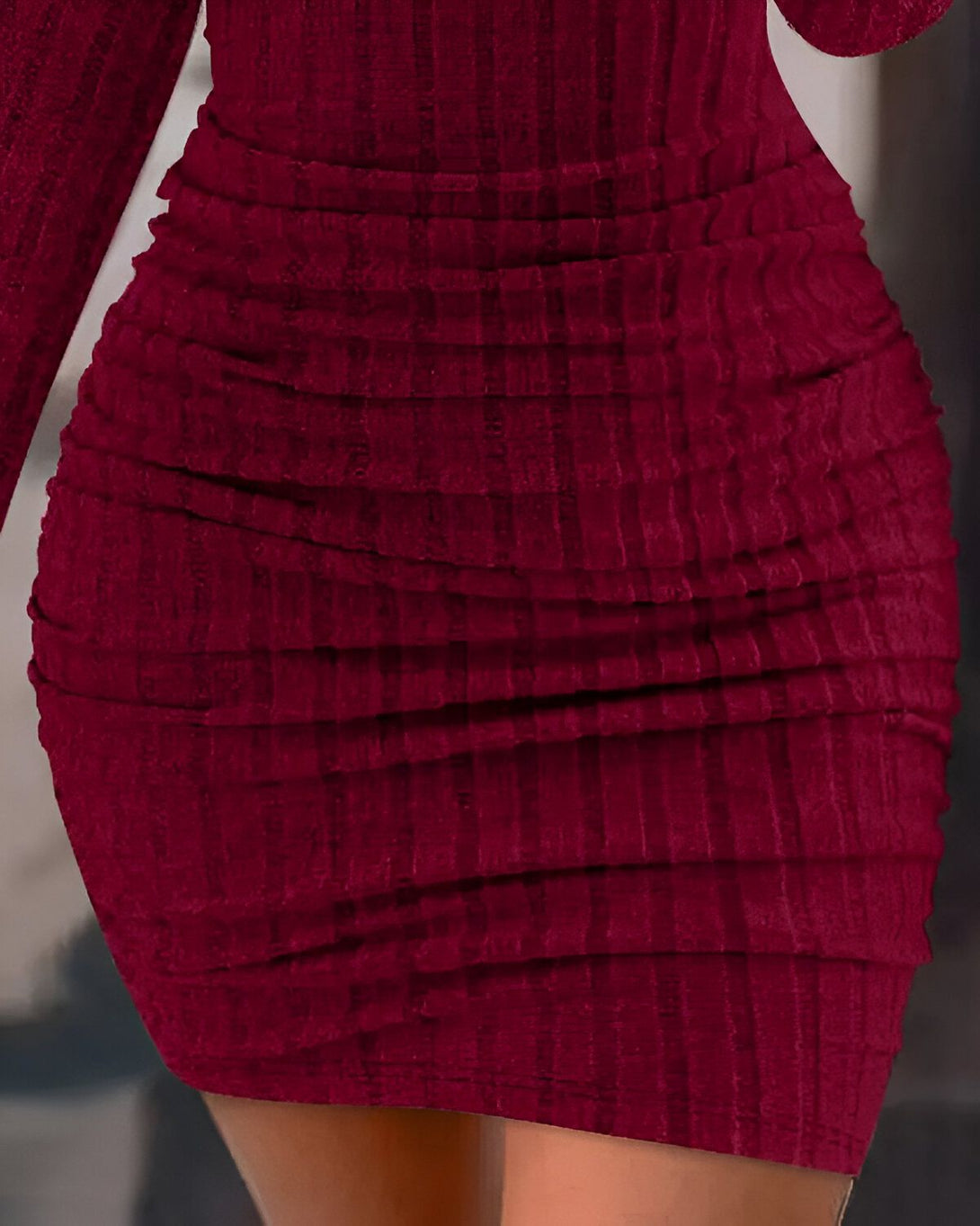 Une femme porte une robe moulante rouge à manches longues. La robe est froncée sur les côtés et met en valeur les courbes de la femme.