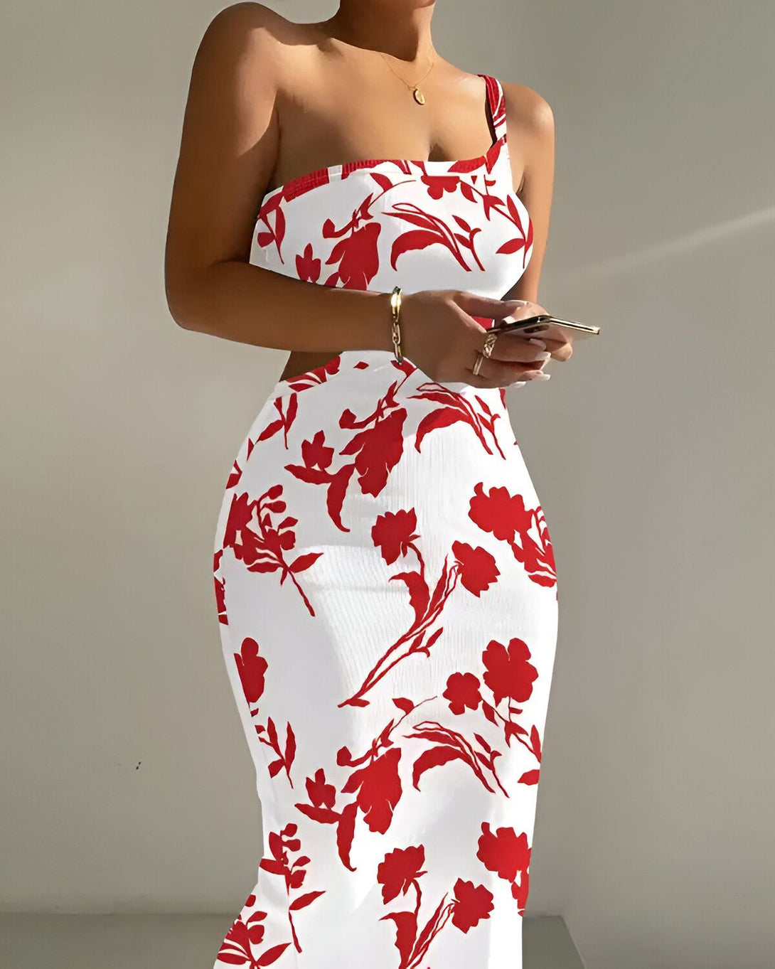 Une femme porte une robe blanche et rouge. La robe est moulante et a une seule bretelle. La femme est debout et tient son téléphone portable.
