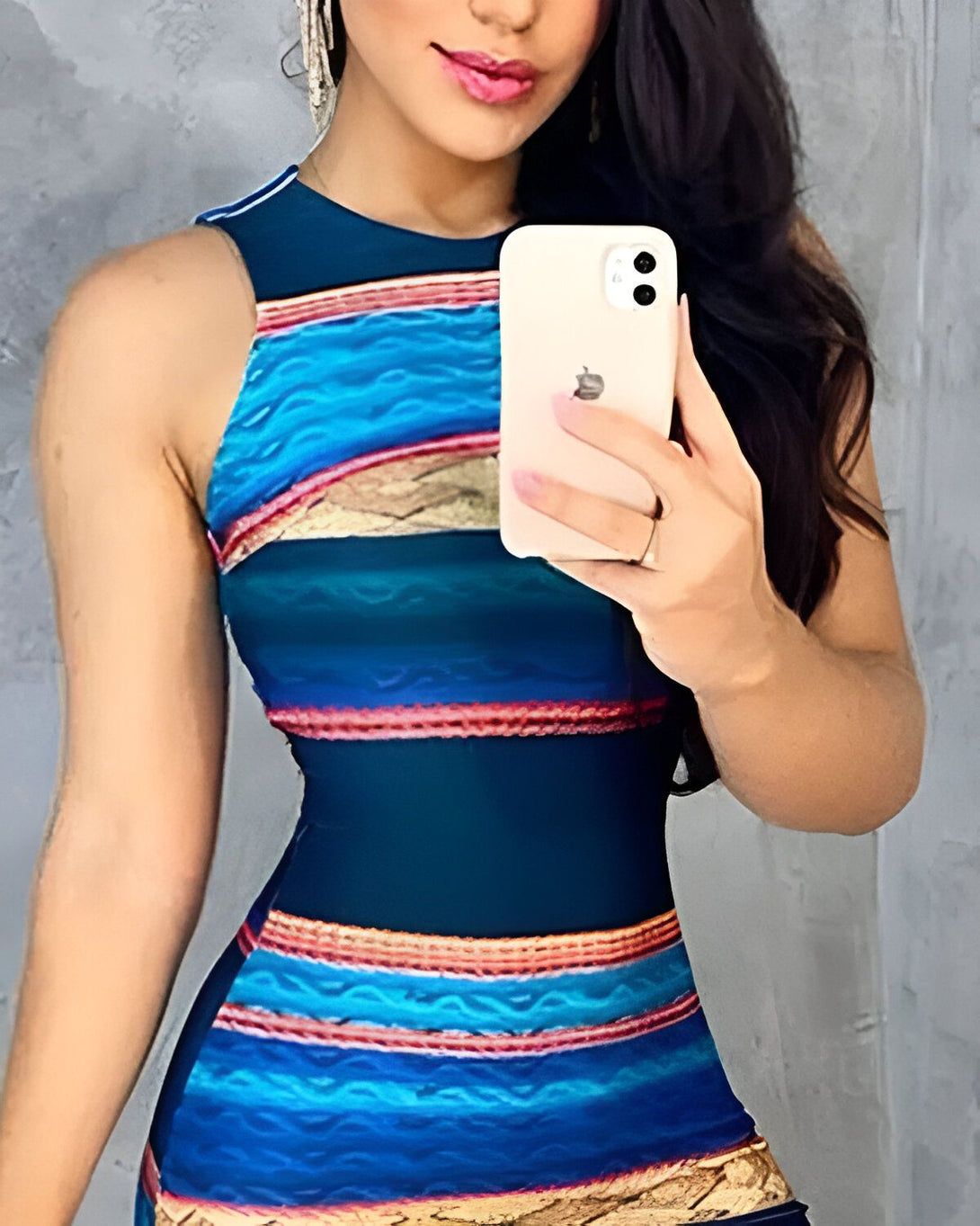 Une femme prend un selfie dans une robe moulante à rayures bleues, vertes et orange. Elle a les cheveux longs et noirs et porte du maquillage.