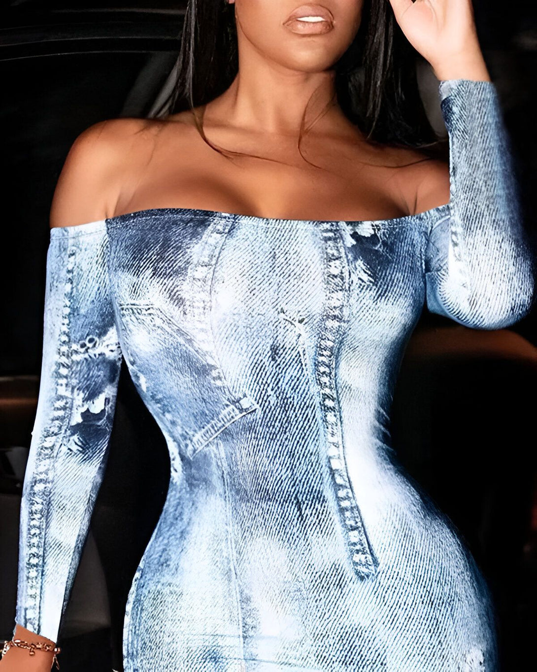 Une femme porte une robe moulante en jean. La robe est sans bretelles et a un décolleté plongeant. La femme est assise dans une voiture et porte des lunettes de soleil.