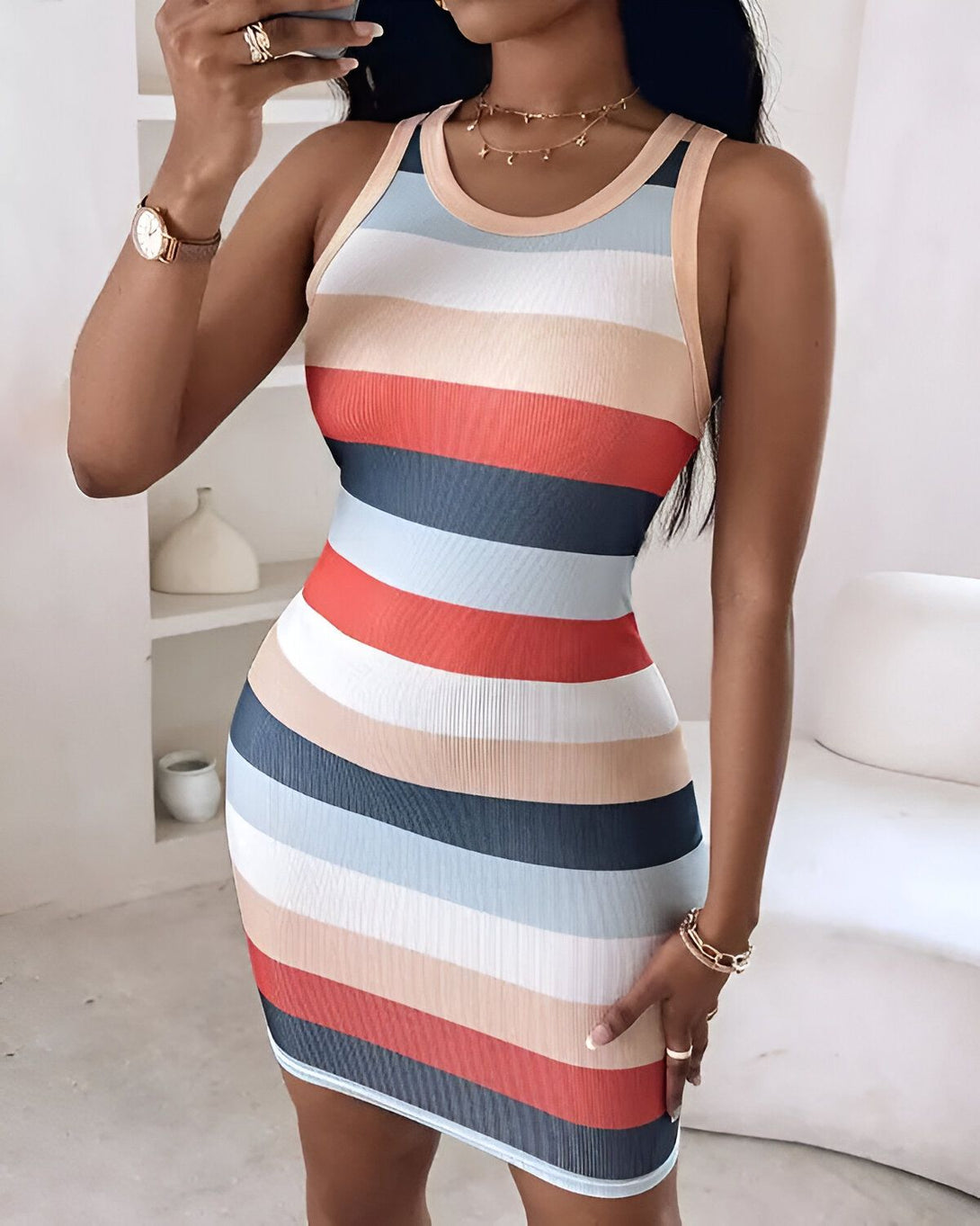 Une femme porte une robe moulante à rayures horizontales multicolores. La robe est courte et sans manches. La femme est debout dans une pièce et se prend en photo dans un miroir.