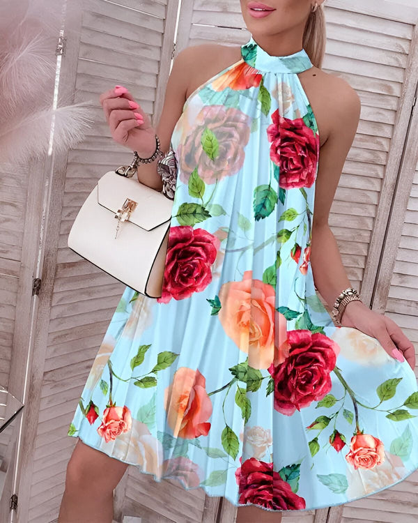 Une femme porte une robe trapèze bleu clair à motif de roses rouges et oranges. La robe est courte et évasée, avec un col montant et des bretelles fines. La femme porte également un sac à main blanc et des talons hauts.