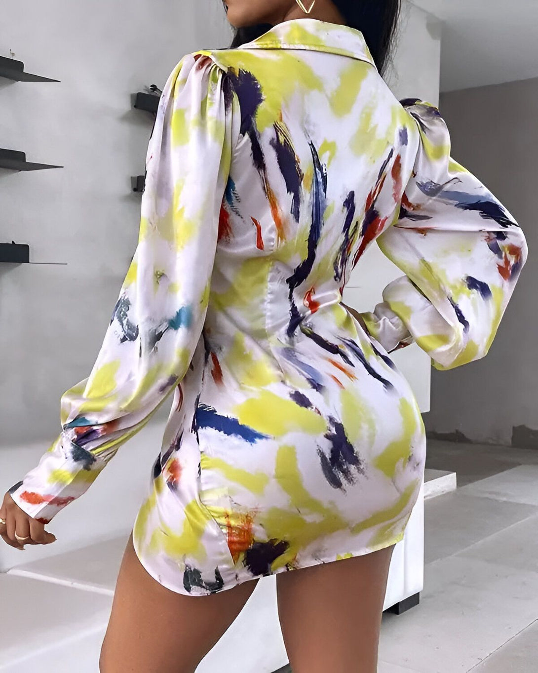 Une femme porte une robe moulante blanche et jaune. La robe est imprimée de motifs abstraits et colorés. La femme est vue de dos.