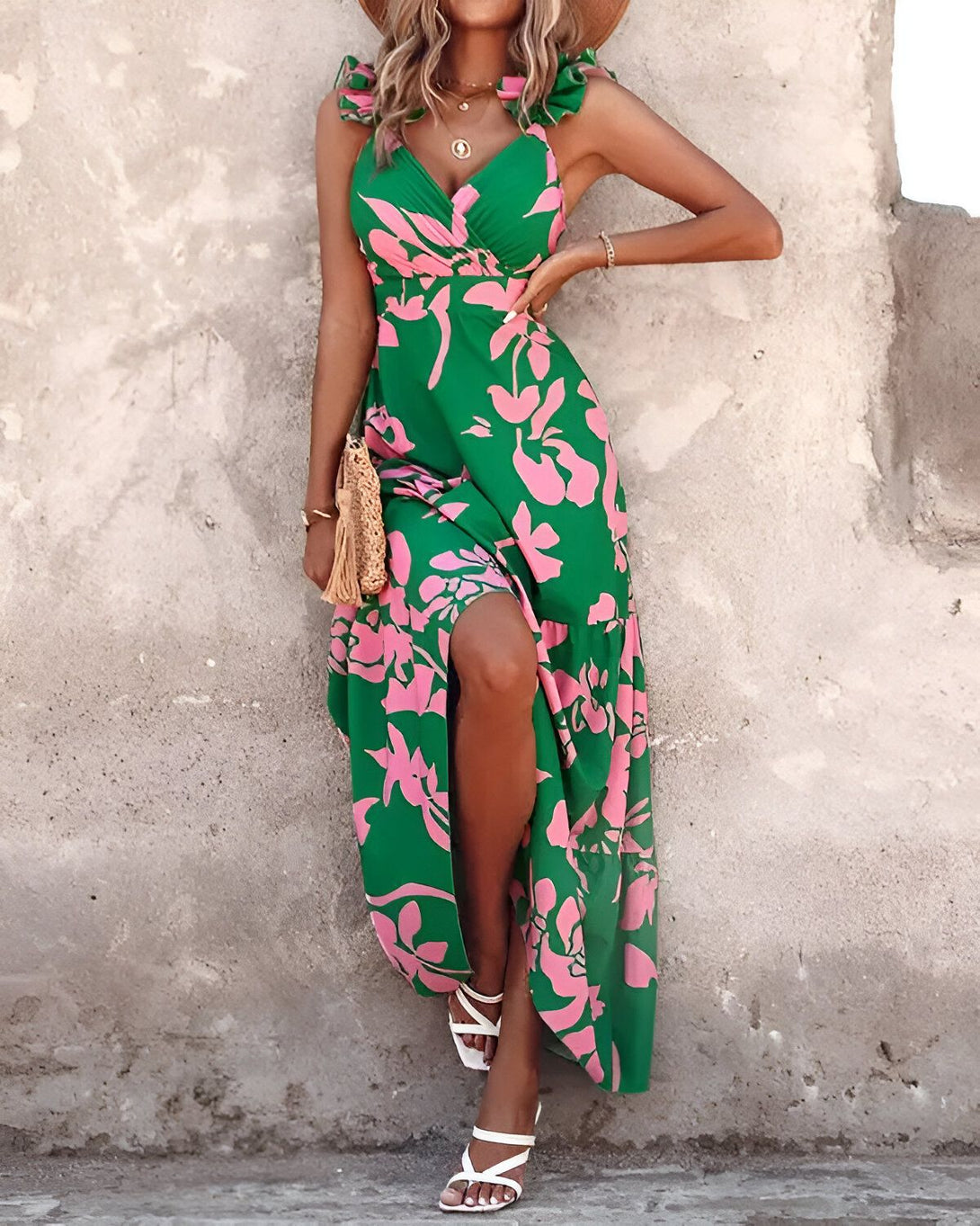 Une femme porte une robe longue verte à motifs floraux roses. Elle est également pieds nus et porte un chapeau de paille.
