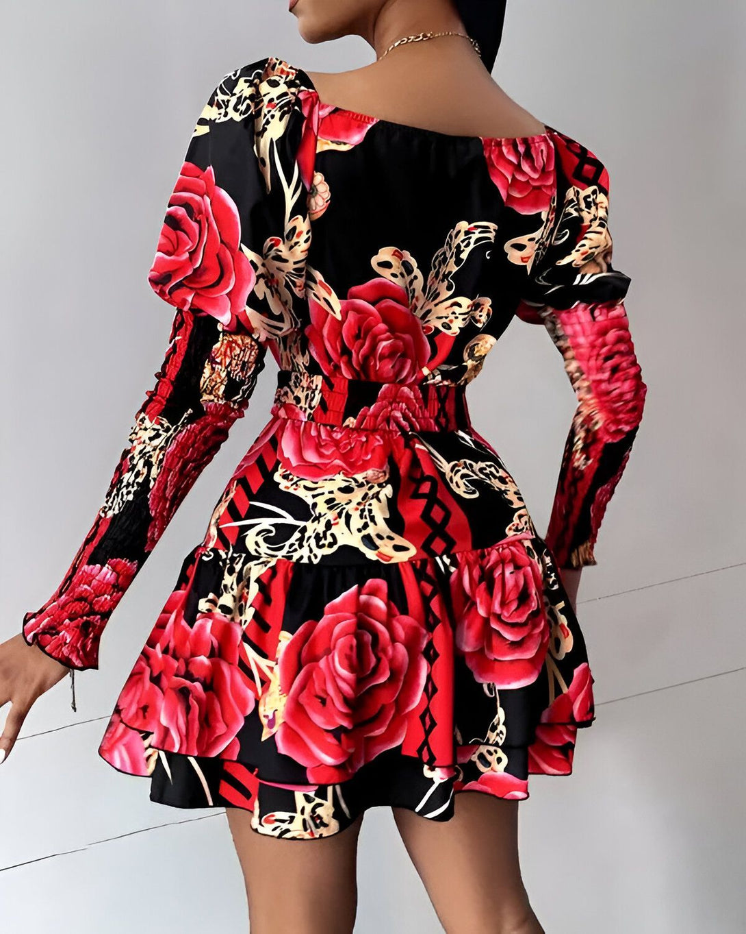 Une femme porte une robe noire à motifs de roses rouges. La robe est courte et évasée, avec des manches bouffantes. La femme est vue de dos.