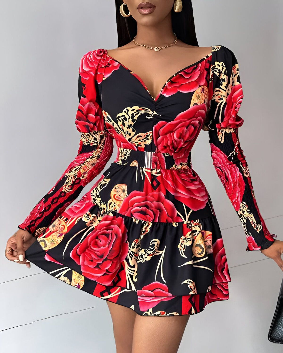 Une femme porte une robe noire et rouge à motifs floraux. La robe est cintrée à la taille et possède un décolleté en V. Les manches sont bouffantes et la jupe est évasée.