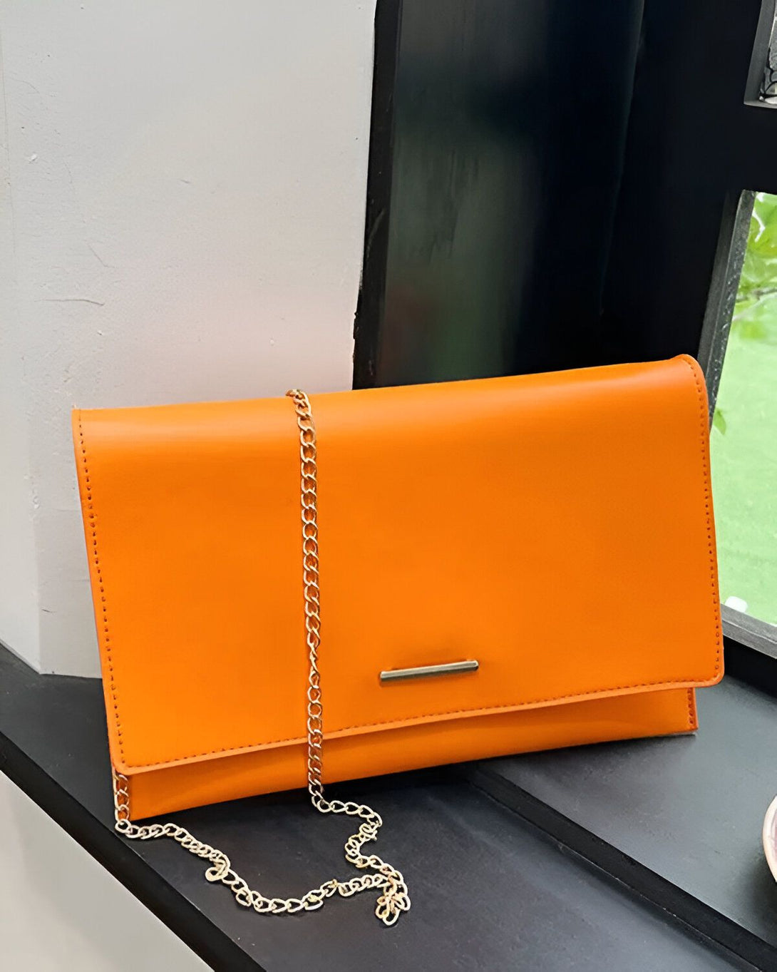 Une image d'un sac à main orange avec une chaîne dorée. Le sac est posé sur une surface noire.