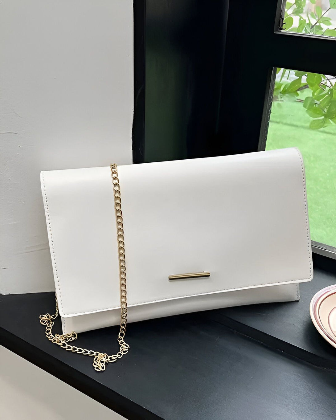 Une image d'un sac à main blanc avec une chaîne en or. Le sac est posé sur une surface noire.