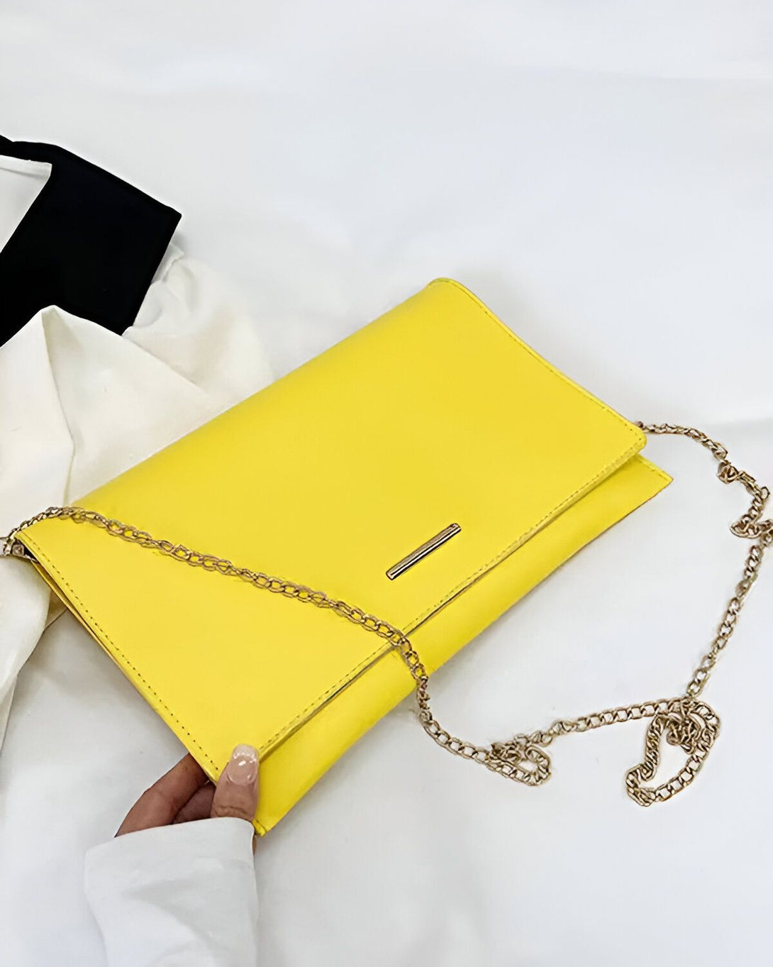 Une image d'un sac à main jaune avec une chaîne dorée. Le sac est porté par une femme vêtue d'une chemise blanche. Le sac est fabriqué en cuir synthétique et possède une doublure en tissu. Il est parfait pour une soirée ou une occasion spéciale.