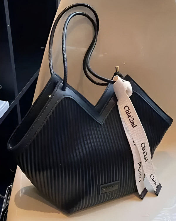 Le sac à main est de couleur noire et possède une anse noire. Il est de forme trapèze et possède un soufflet sur le côté. Le sac est en matière synthétique et possède une doublure en tissu. Il est de taille moyenne et peut contenir une grande quantité d'affaires. Le sac est parfait pour une utilisation quotidienne ou pour une sortie.