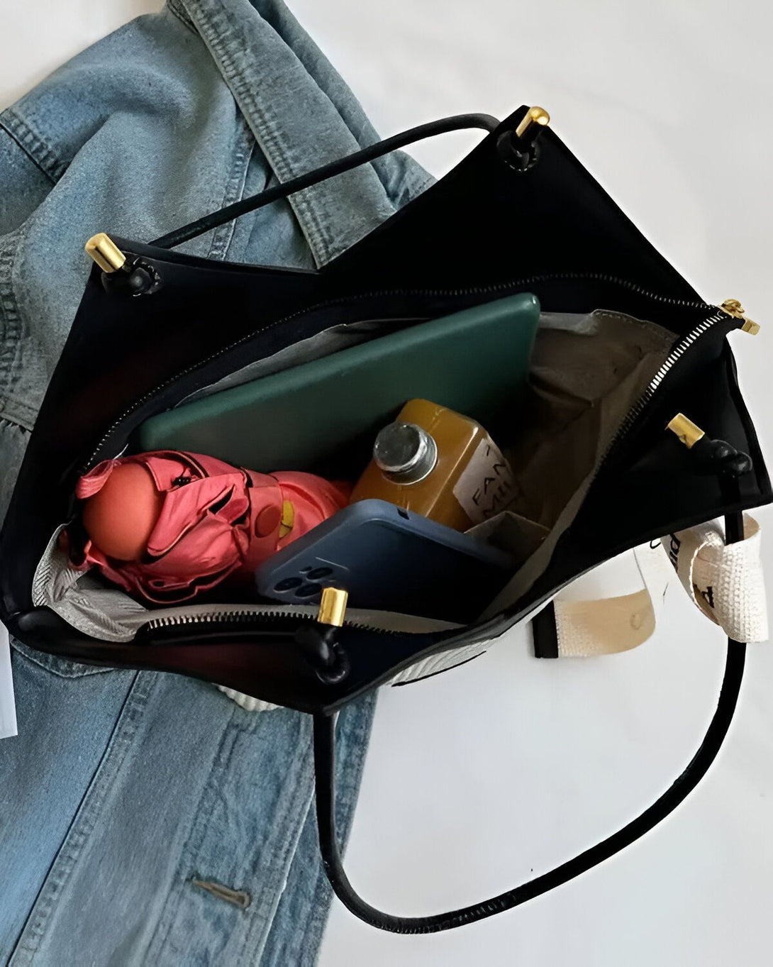 Un sac à main noir ouvert avec à l'intérieur un téléphone portable, un portefeuille, des clés et un parapluie rose.