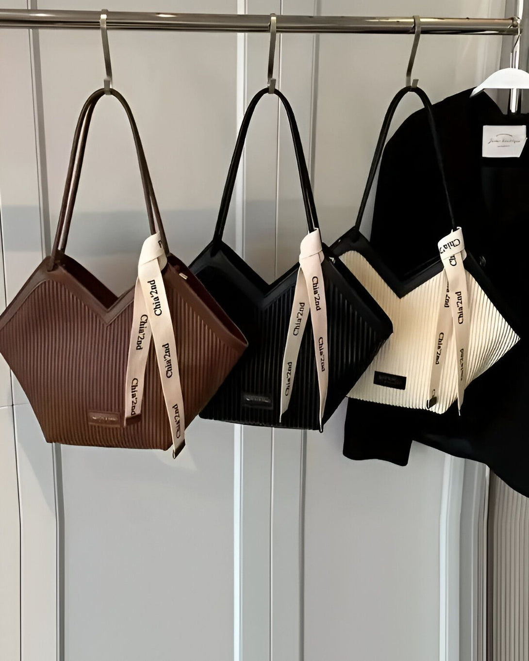 Trois sacs à main en cuir marron, noir et blanc sont suspendus à une tringle. Les sacs sont de la marque "Chiaz2nd".