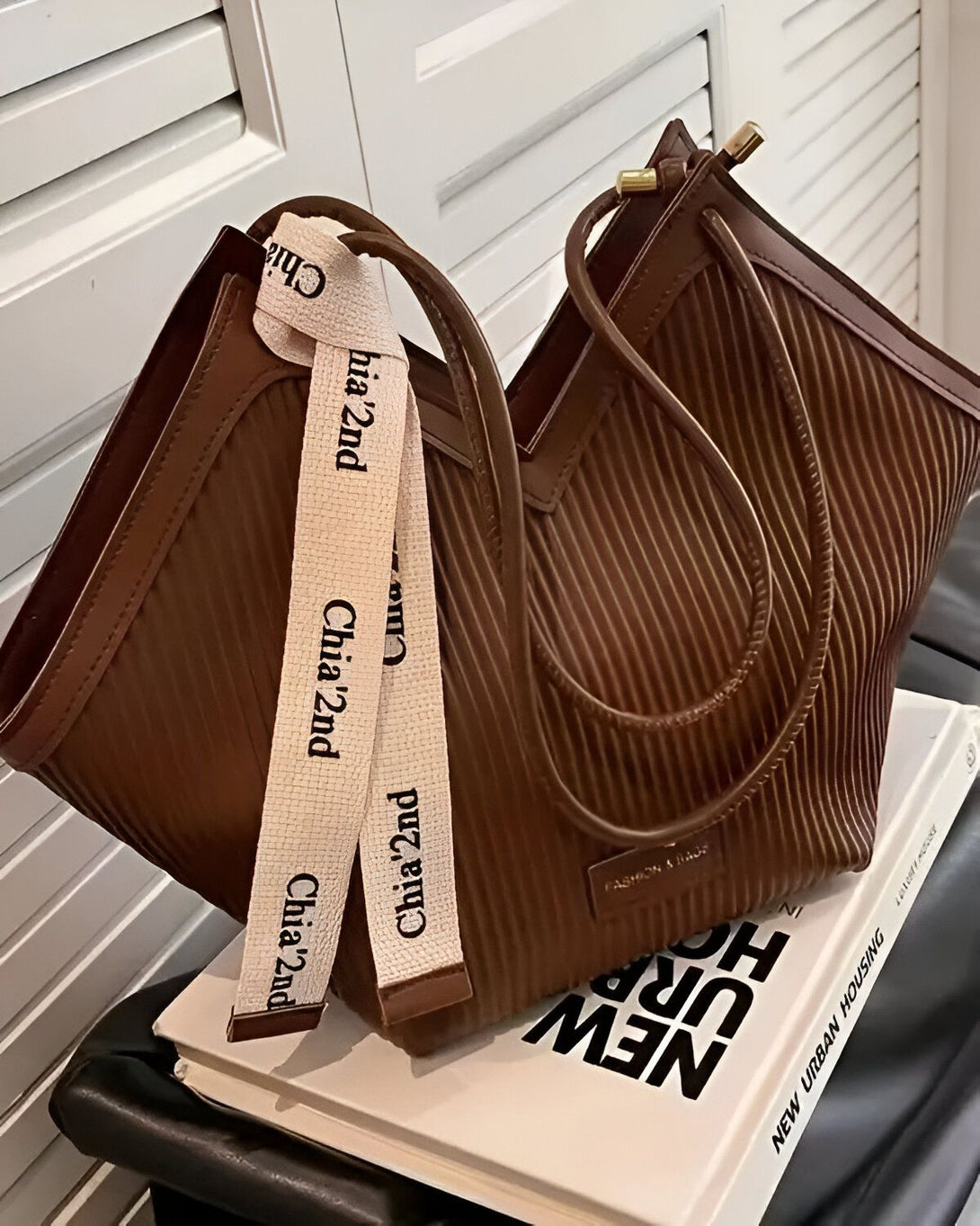 Un sac à main marron avec une anse blanche et marron. Le sac est posé sur un livre ouvert.