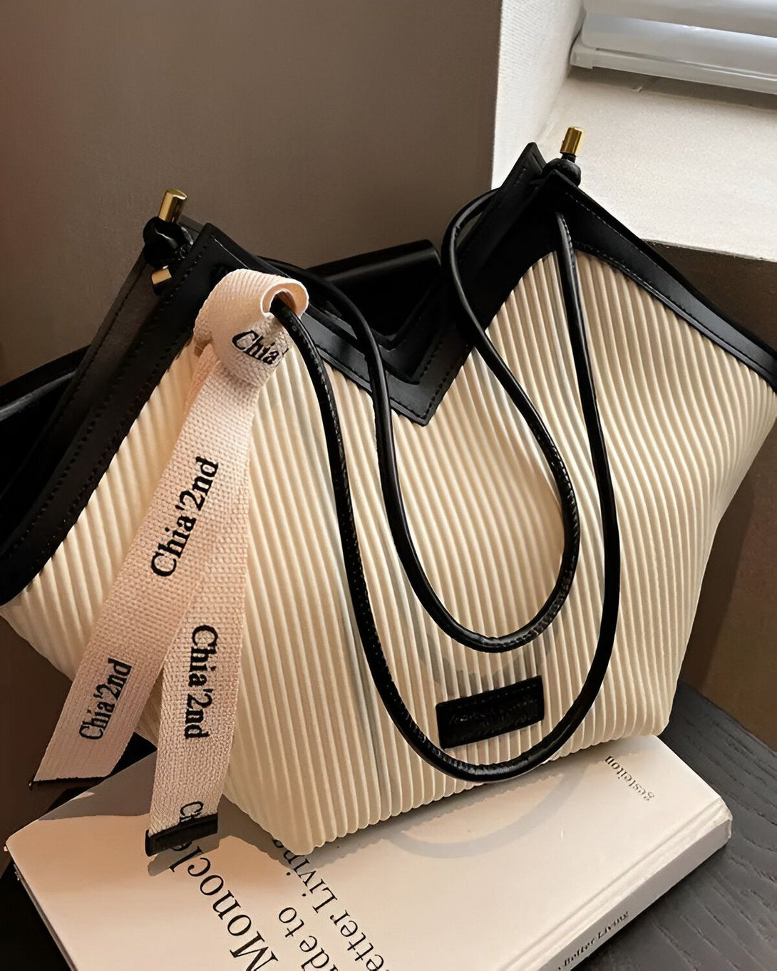 Un sac à main blanc cassé avec des anses noires et un ruban noir et blanc avec le logo "Chiaz2nd" dessus.