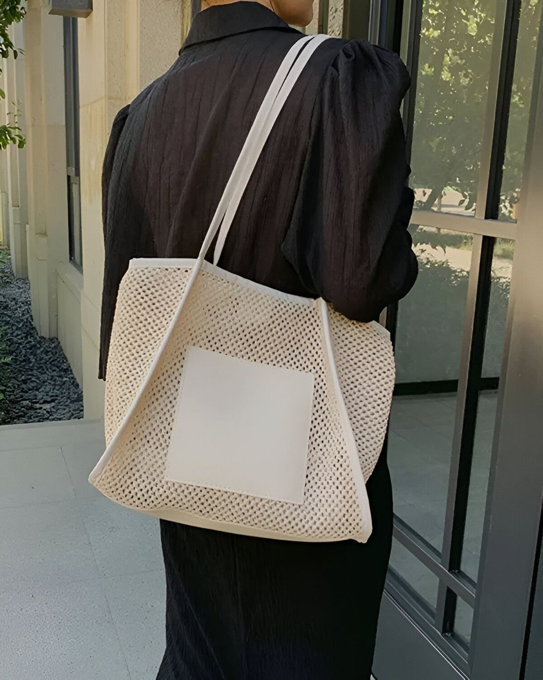 Une femme porte une robe noire et un sac à main beige avec une grande anse. Le sac à main est en filet et possède une poche avant rectangulaire en cuir blanc.