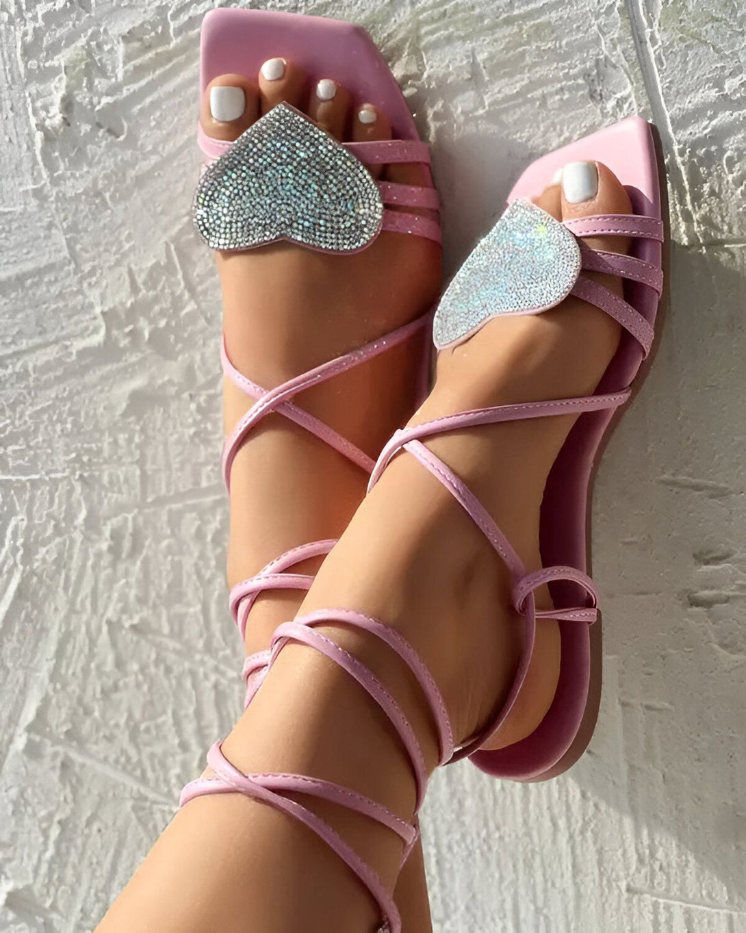 Une femme porte des sandales roses à talons hauts avec des cœurs en strass. Les sandales sont attachées aux chevilles par des lanières roses.