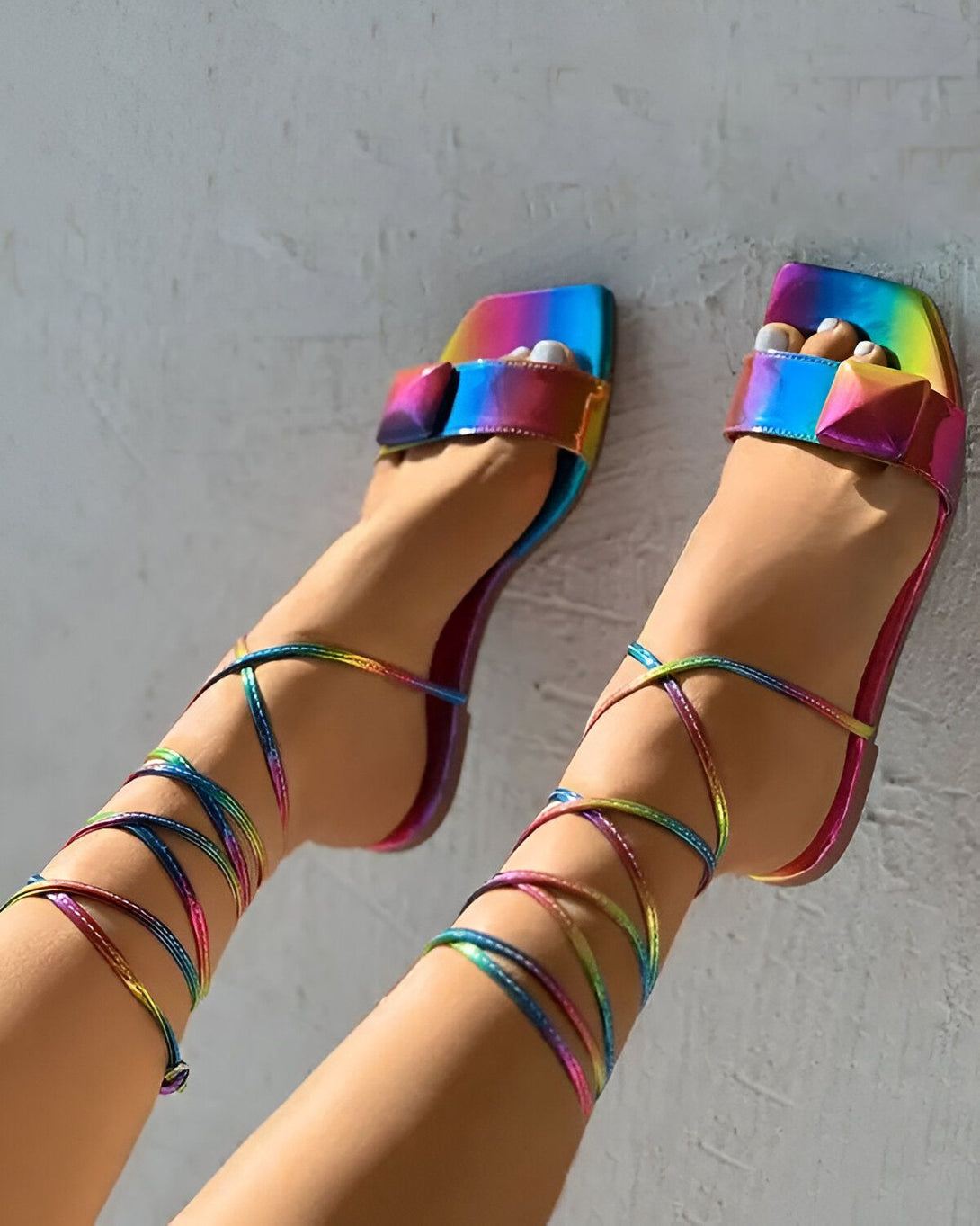 Une femme porte des sandales à talons hauts multicolores. Les sandales sont attachées aux chevilles par des lanières arc-en-ciel.