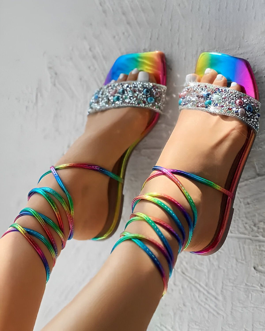 Une femme porte des sandales arc-en-ciel à talons hauts avec des brides à lacets qui s'enroulent autour de ses jambes. Les sandales sont ornées de strass et de perles.