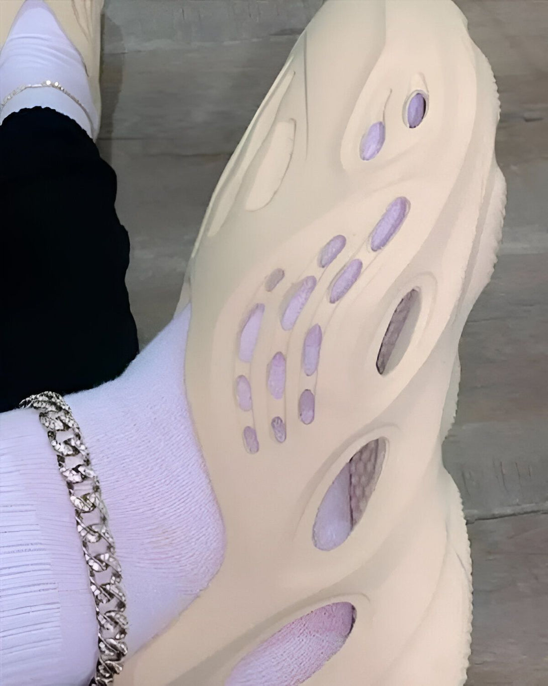 Une personne porte des sandales beige trouées avec des chaussettes montantes blanches et un pantalon noir.