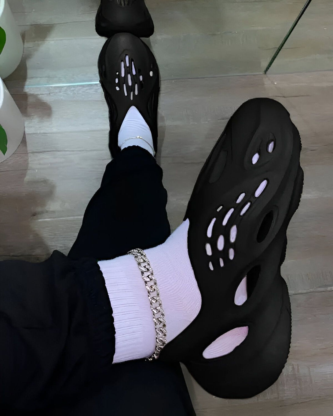 Une personne porte des chaussettes blanches, un pantalon noir et des sandales noires trouées.