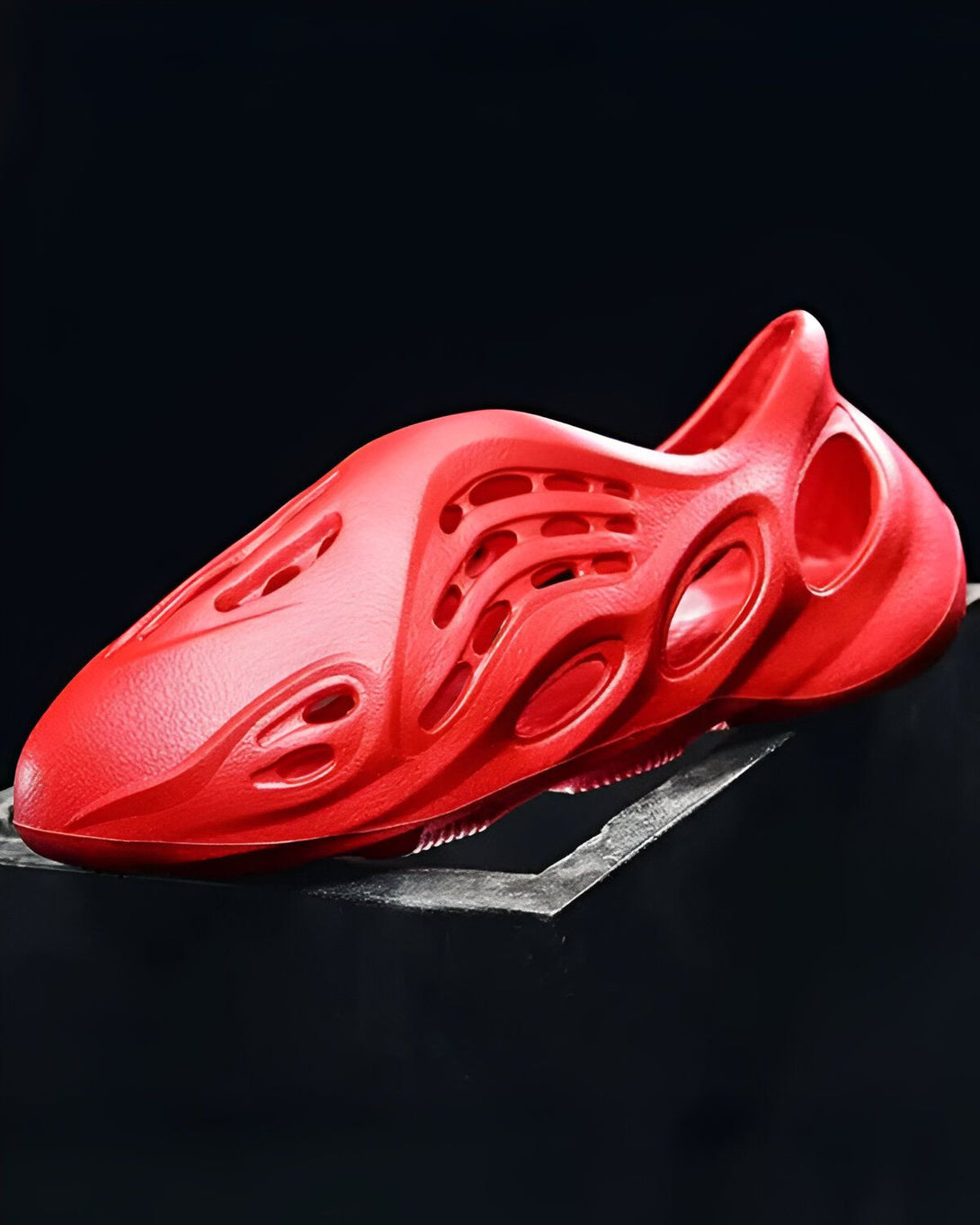 Une image d'une paire de sabots rouges en mousse. Les sabots ont des trous sur le dessus et sont posés sur une surface noire.
