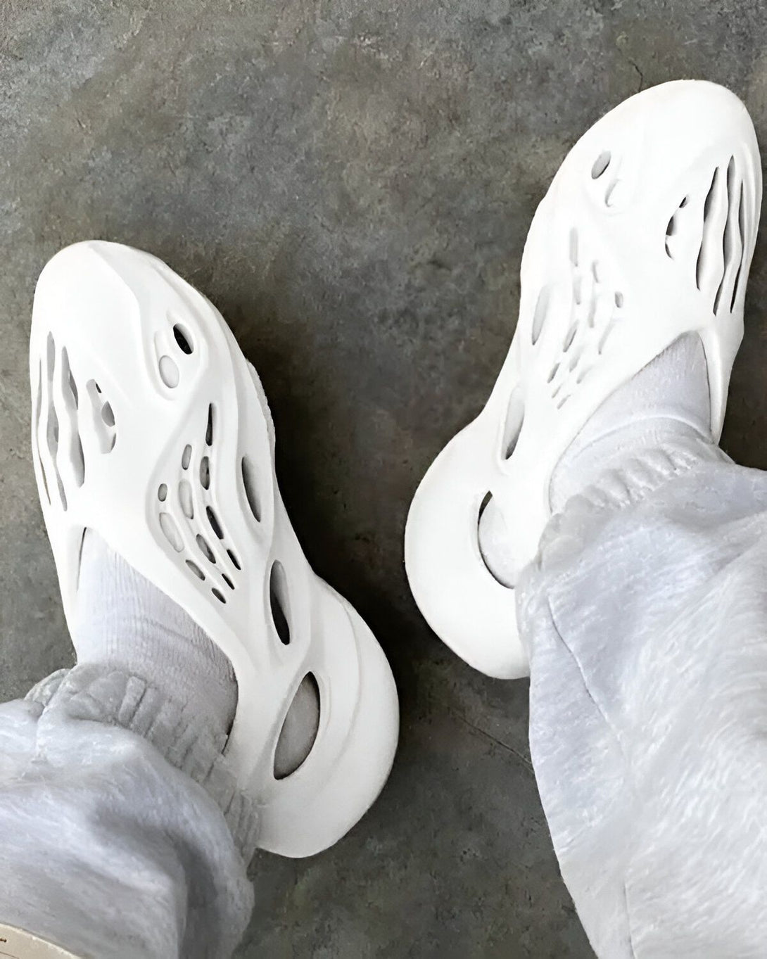Une paire de chaussures Yeezy Foam Runner blanche est posée sur un sol en béton gris.