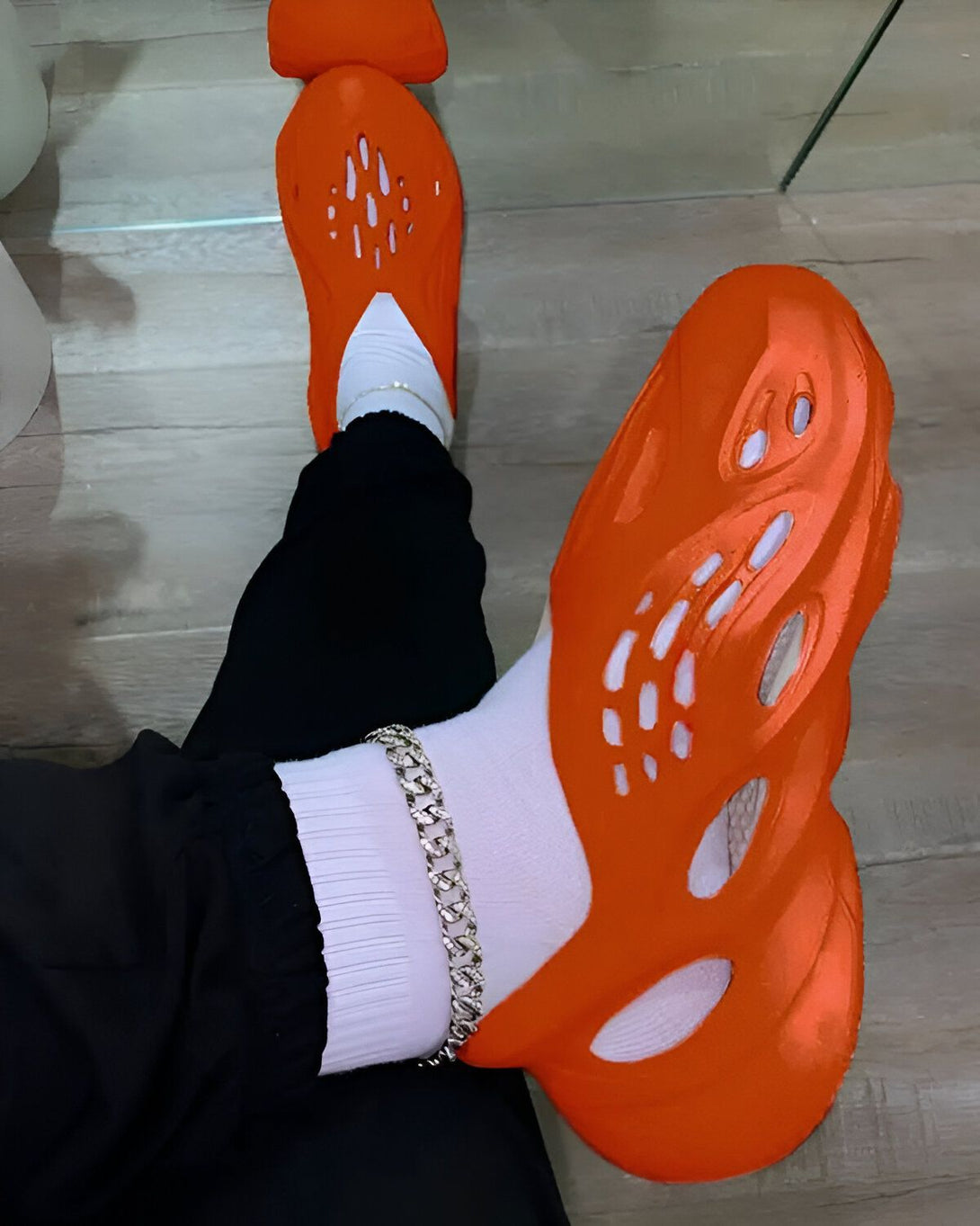 Une personne porte des chaussettes blanches, un pantalon noir et des Crocs orange.