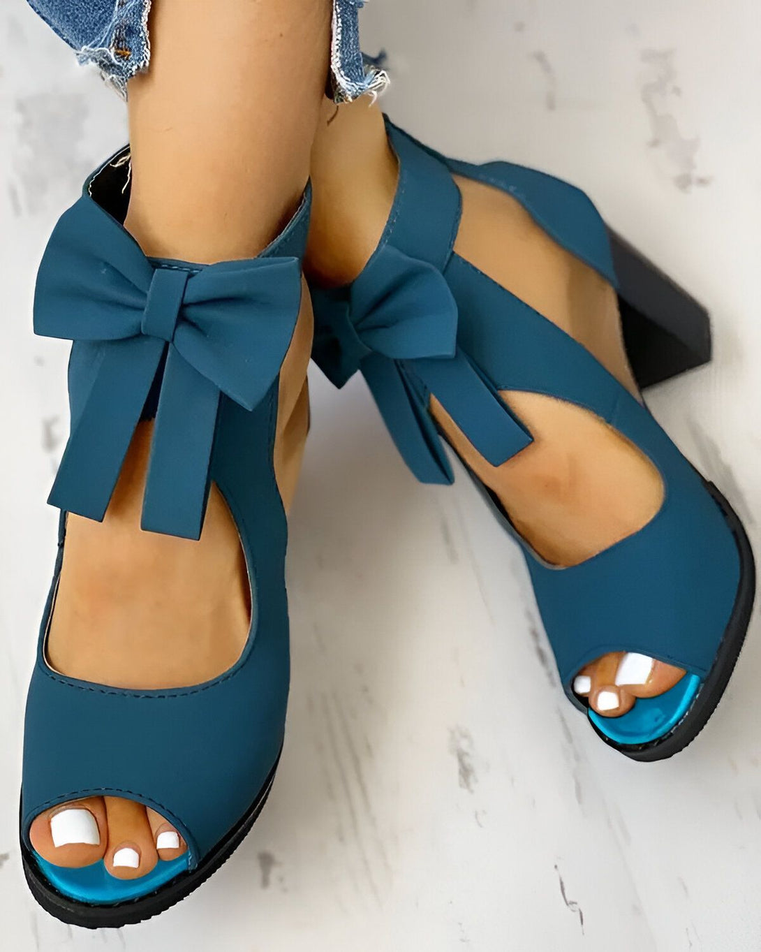 Une femme porte des sandales à talons hauts bleues. Les sandales ont un nœud sur le devant et sont ouvertes au niveau des orteils. La femme a les ongles des pieds peints en blanc.