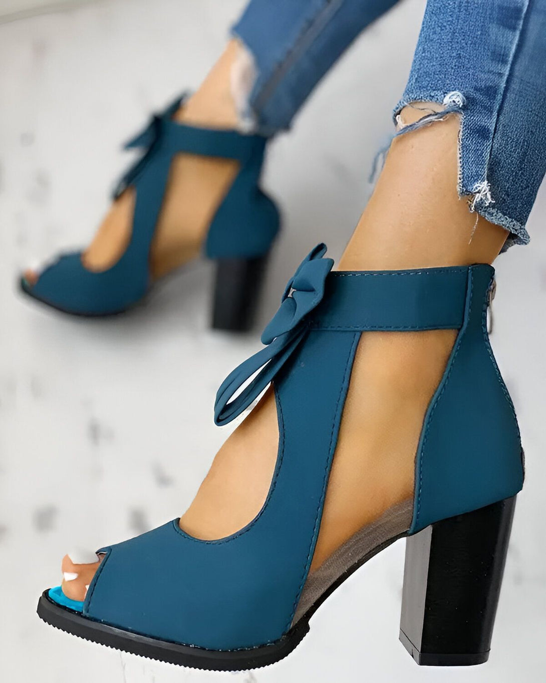 Une femme porte des chaussures à talons hauts bleues. Les chaussures sont ouvertes au niveau des orteils et ont un nœud sur le dessus. La femme porte un jean bleu et les chaussures sont assorties à la couleur de ses ongles.