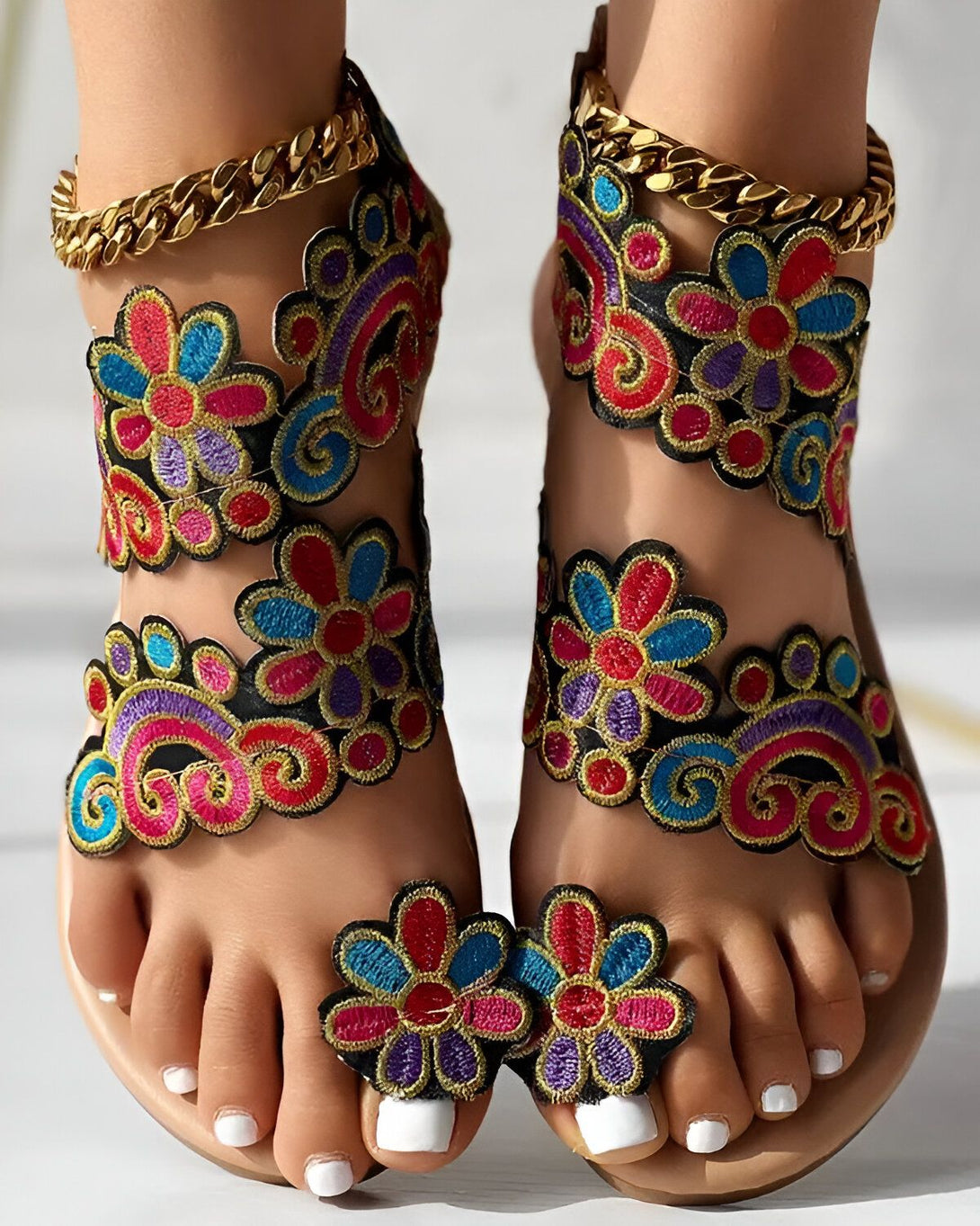 Une paire de sandales plates brodées de fleurs colorées avec des brides cheville dorées.