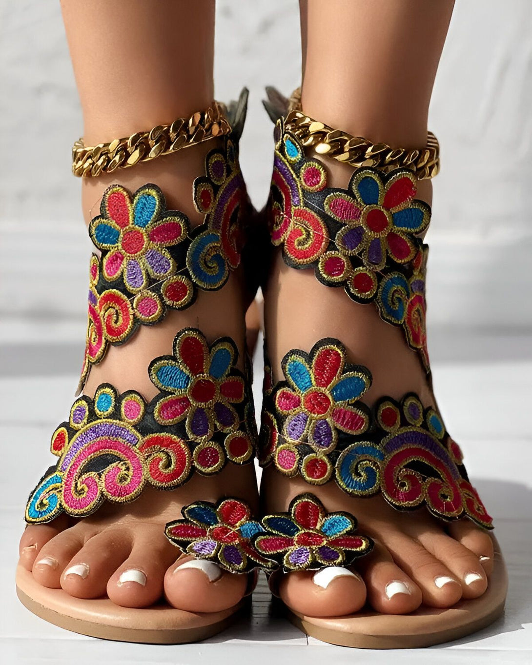 Une paire de sandales plates brodées de fleurs colorées avec des brides cheville et des semelles en cuir.