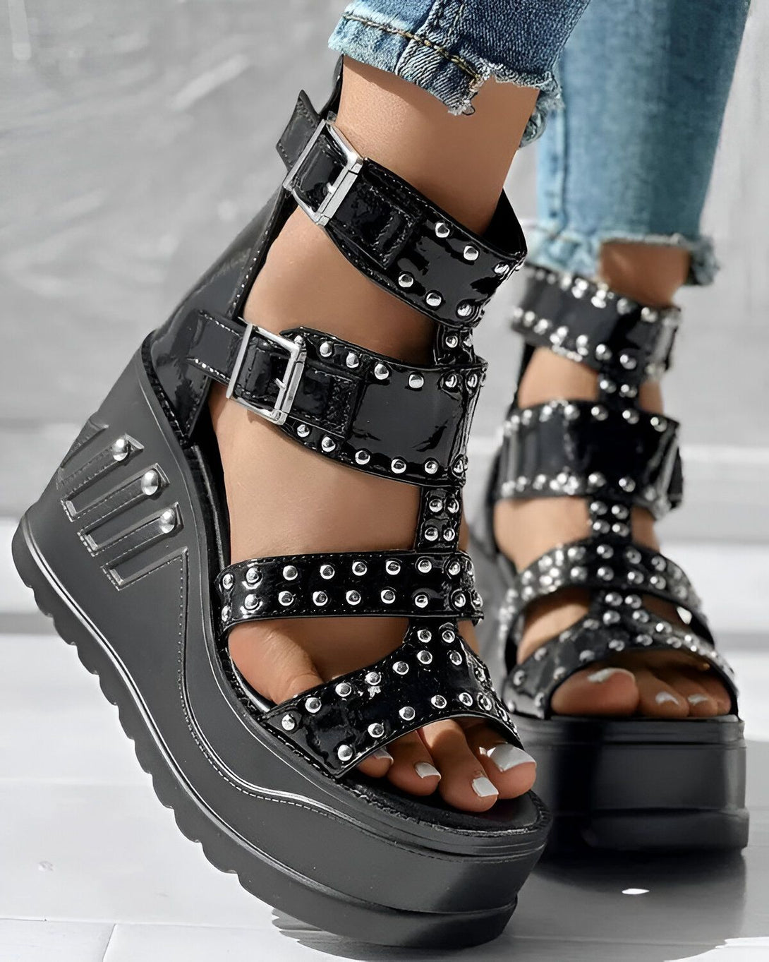 Une image de sandales compensées noires à talons hauts avec des brides à boucles et des clous argentés.