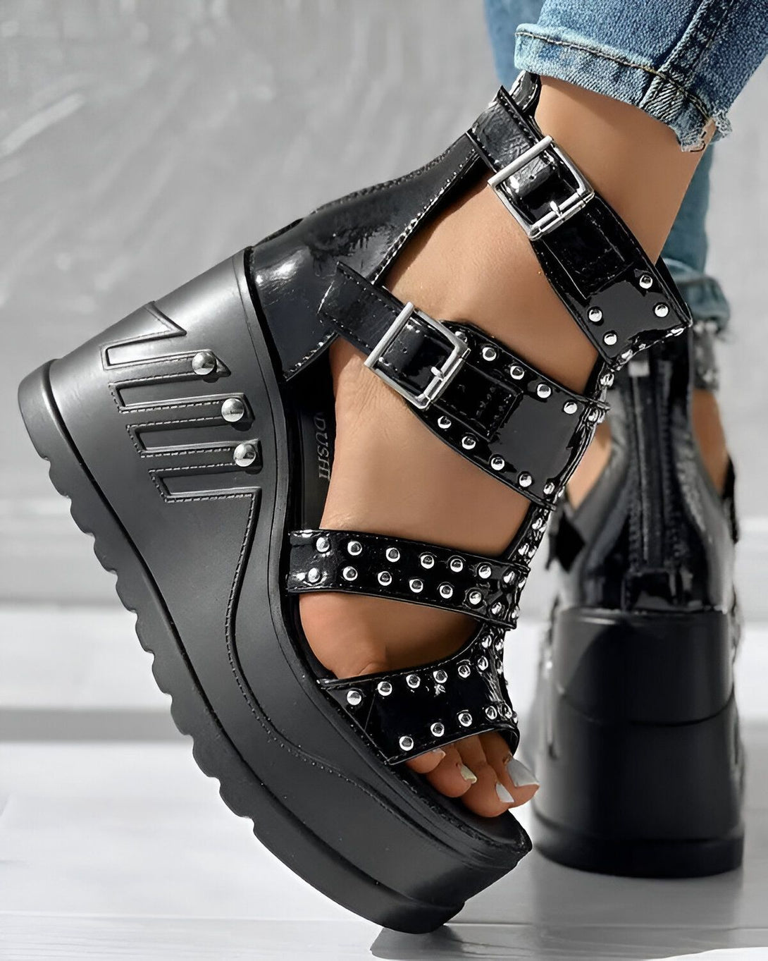 Une image d'une paire de sandales compensées noires à talons hauts avec des brides à boucles et des clous argentés.