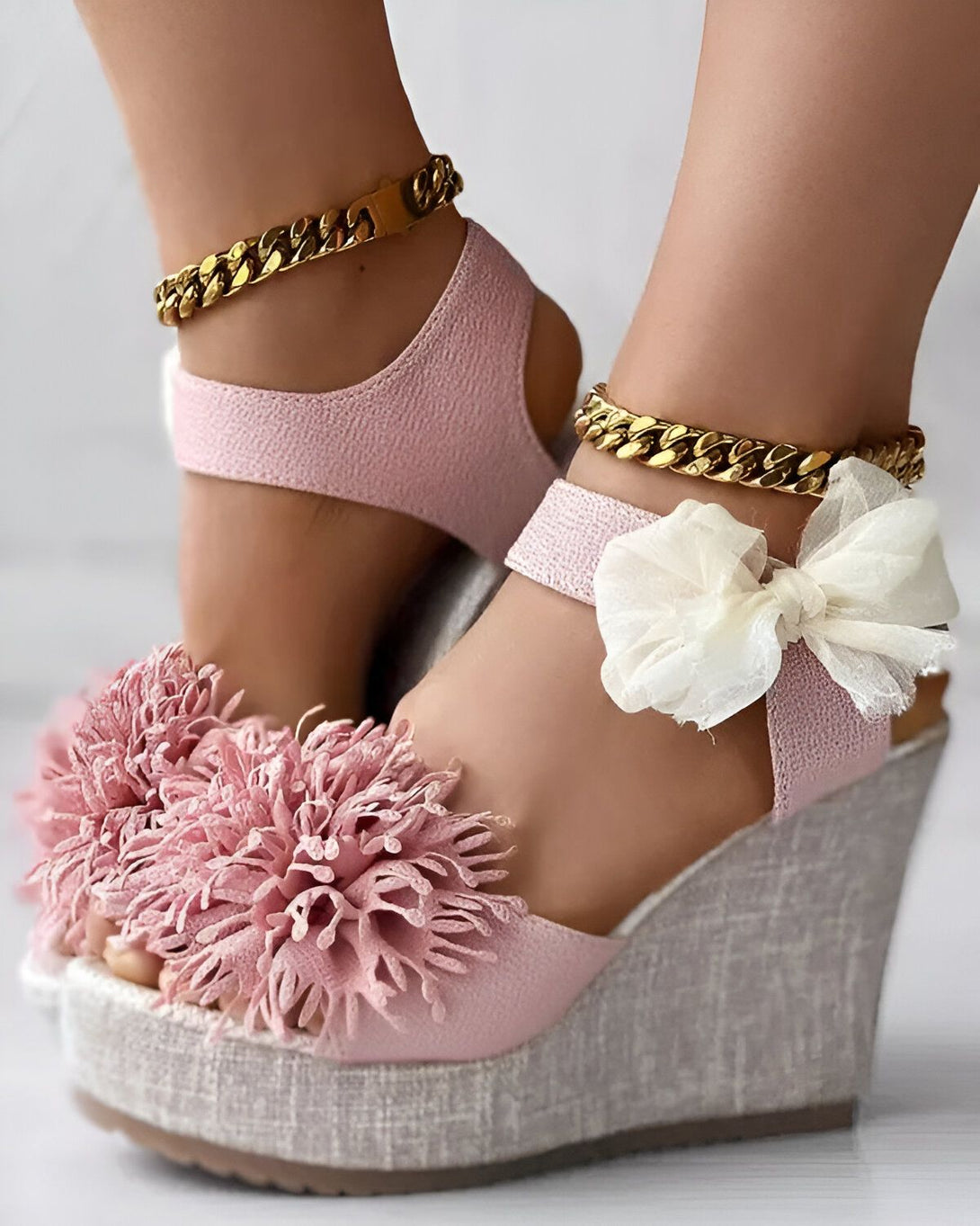 Une paire de sandales compensées roses à talons hauts avec des brides en chaîne dorées et des nœuds en tissu blanc sur le devant.