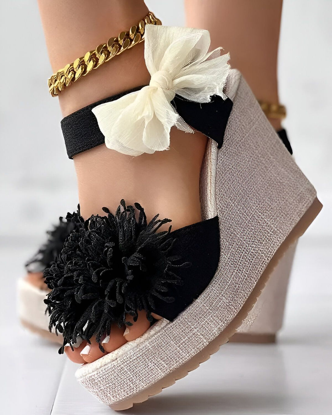Une image d'une paire de sandales compensées noires et blanches à talons hauts. Les sandales sont ornées d'un nœud en tissu blanc et noir et de fleurs en tissu noir.