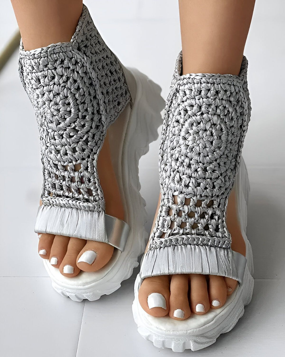 Une paire de sandales compensées en crochet argentées avec des brides cheville.