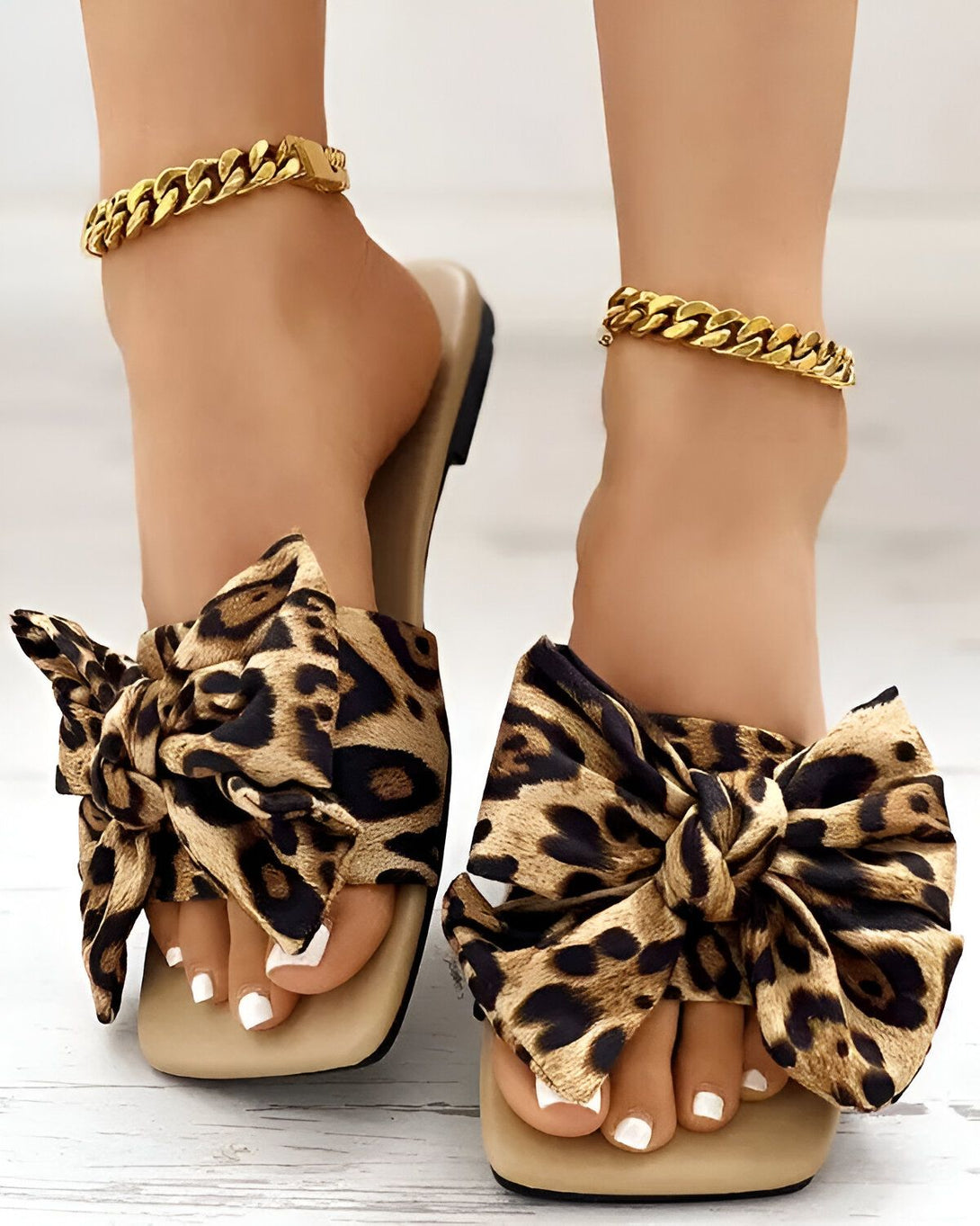 Une femme porte des sandales à talons hauts avec un nœud en tissu léopard. Les sandales sont de couleur beige et marron.