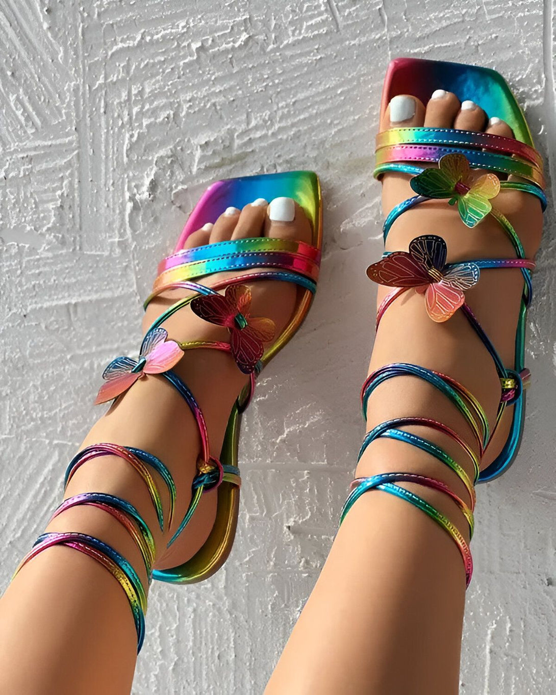 Une femme porte des sandales à talons hauts multicolores. Les sandales sont ornées de papillons en métal.