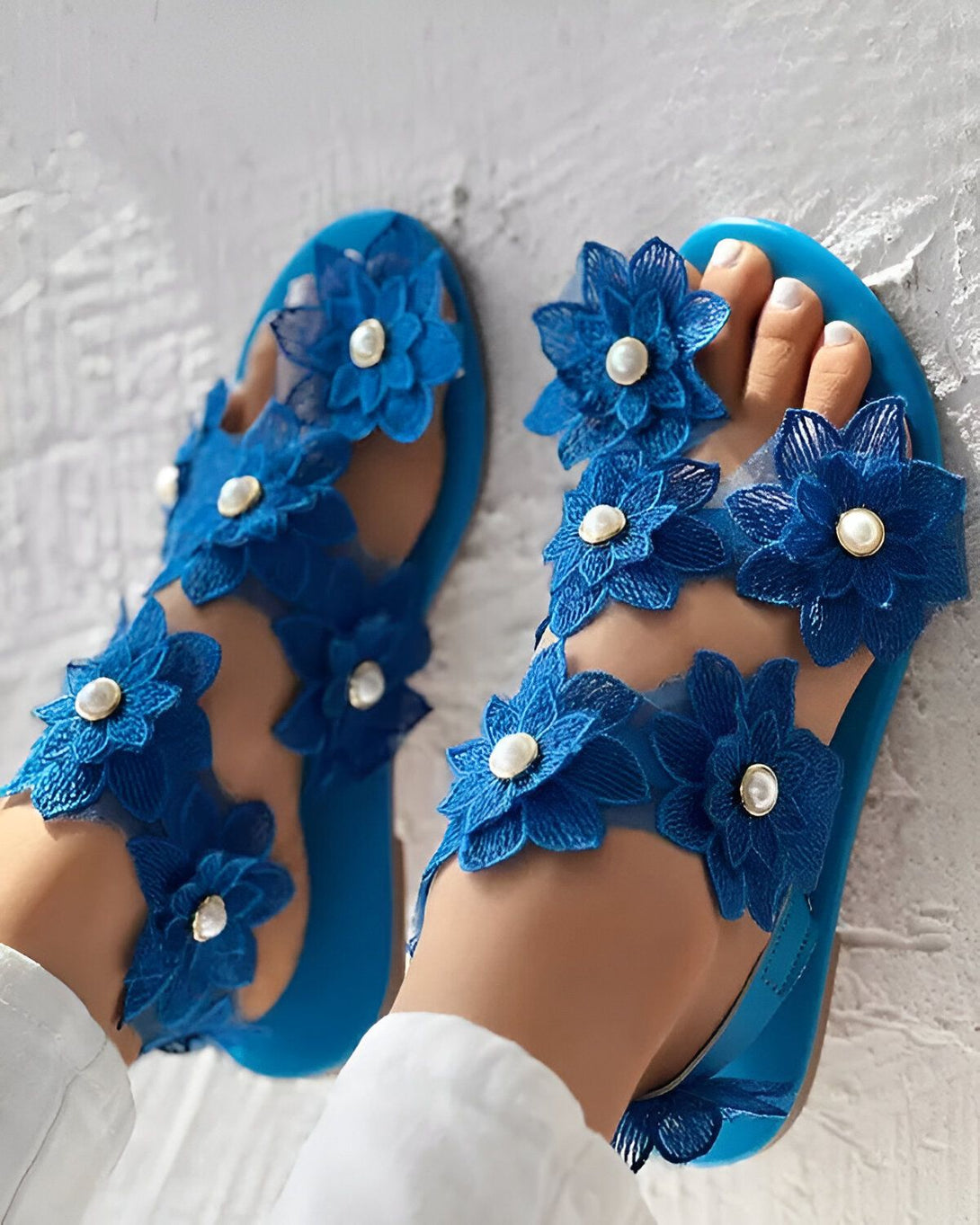 Une paire de sandales plates bleues avec des fleurs en tissu bleu et des perles blanches.