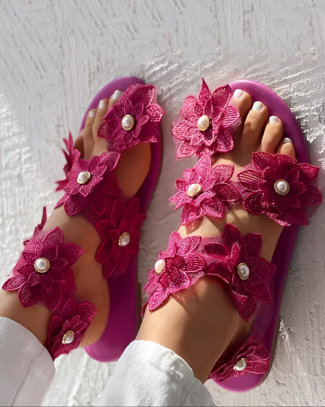 Une paire de sandales roses à talons plats. Les sandales sont ornées de fleurs en tissu rose et de perles blanches.