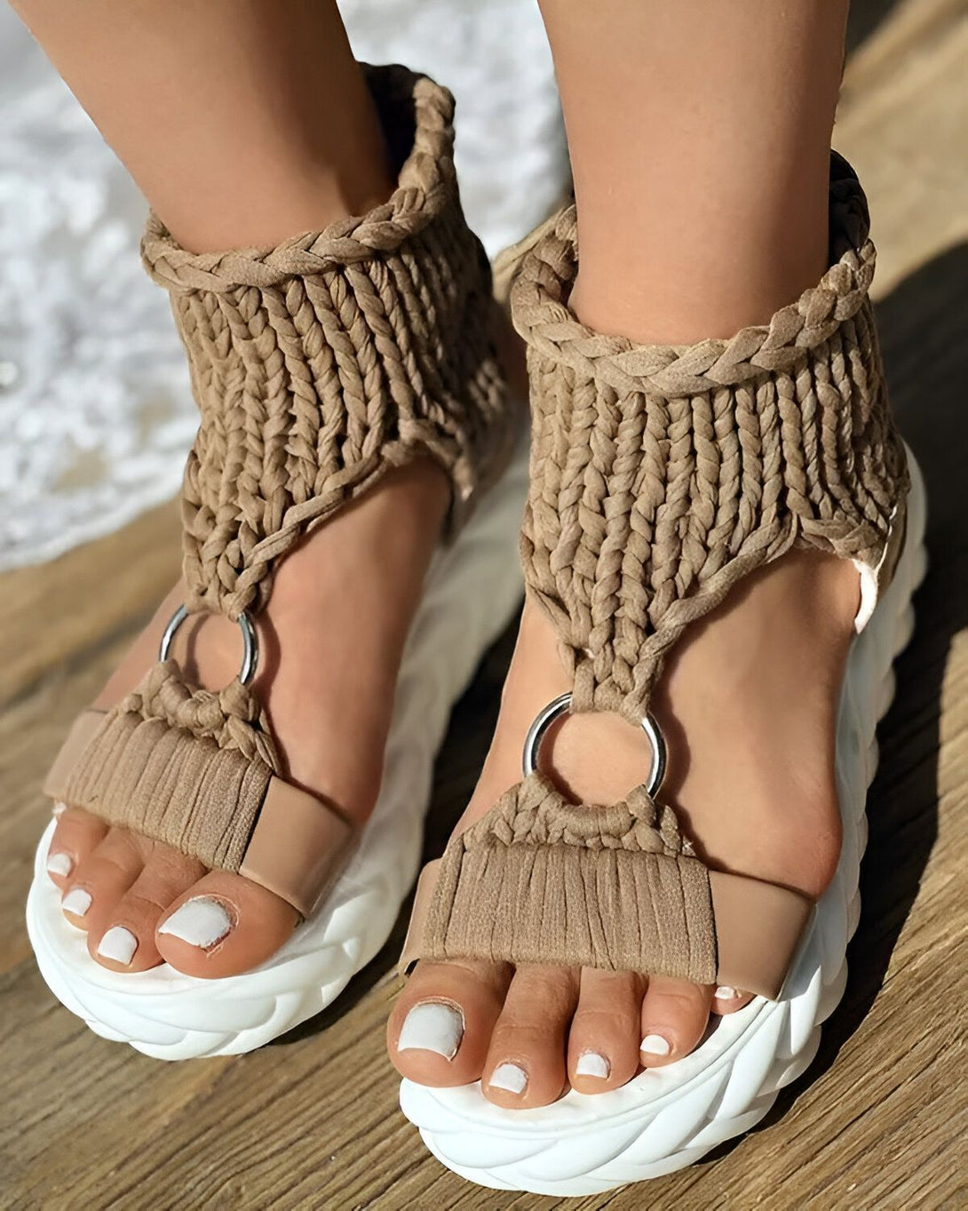 Une femme porte des sandales marron clair avec des semelles compensées blanches. Les sandales sont faites d'un matériau tissé et ont des brides qui s'enroulent autour de la cheville.