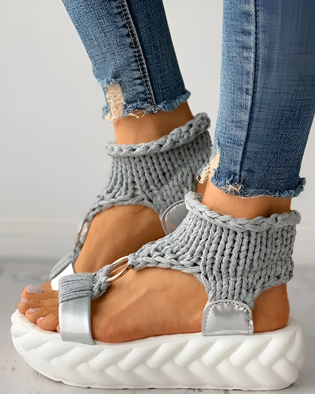 Une femme porte des sandales grises avec des jeans bleus. Les sandales sont en laine et ont une semelle blanche.