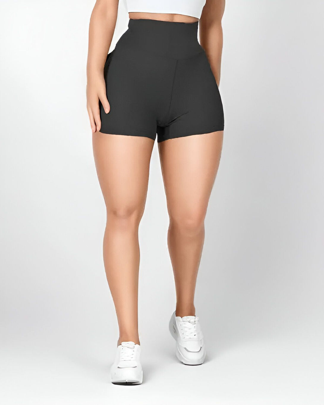 Une femme porte un short moulant noir taille haute avec des baskets blanches.