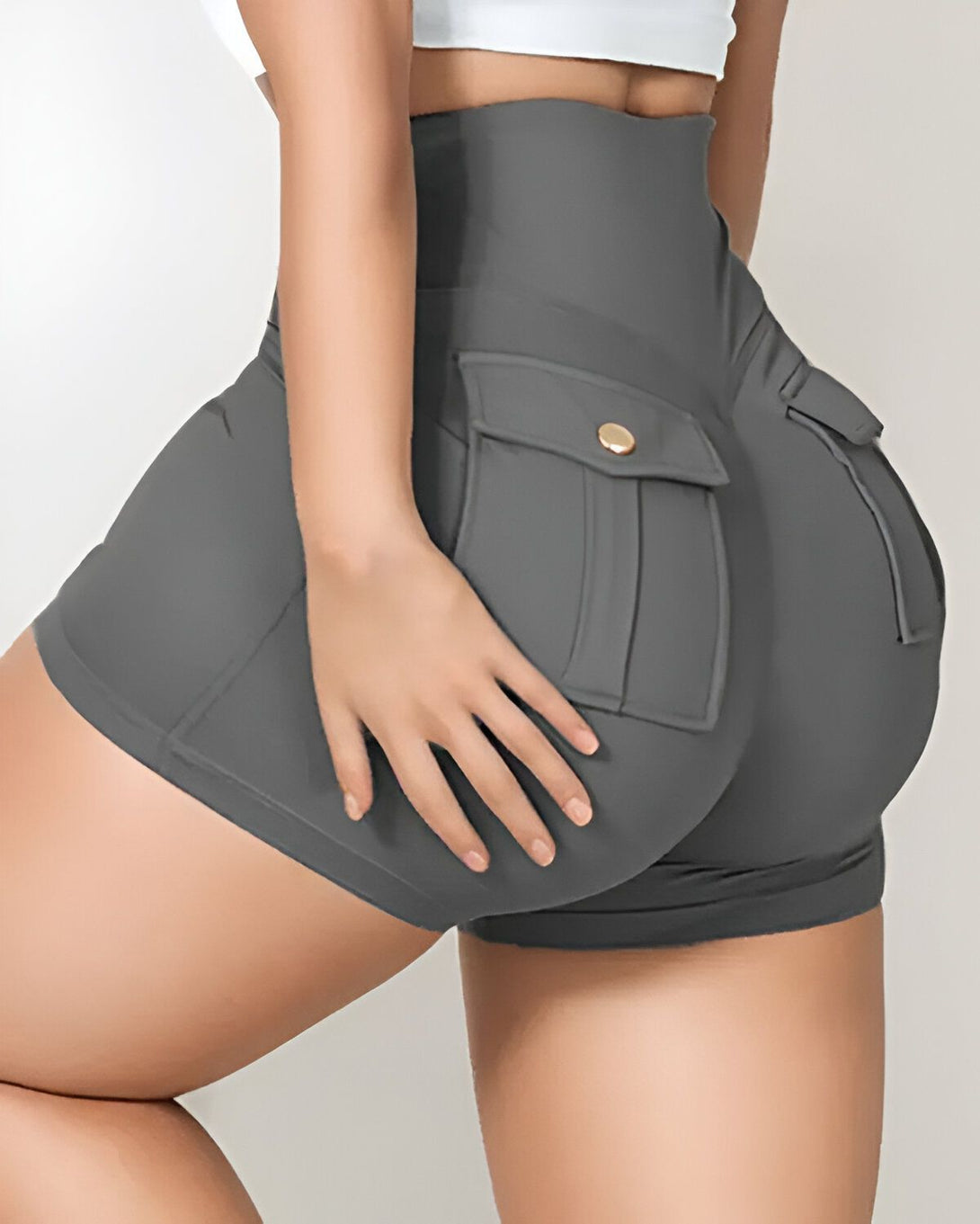 Une femme porte un short moulant gris taille haute avec des poches et des boutons dorés.