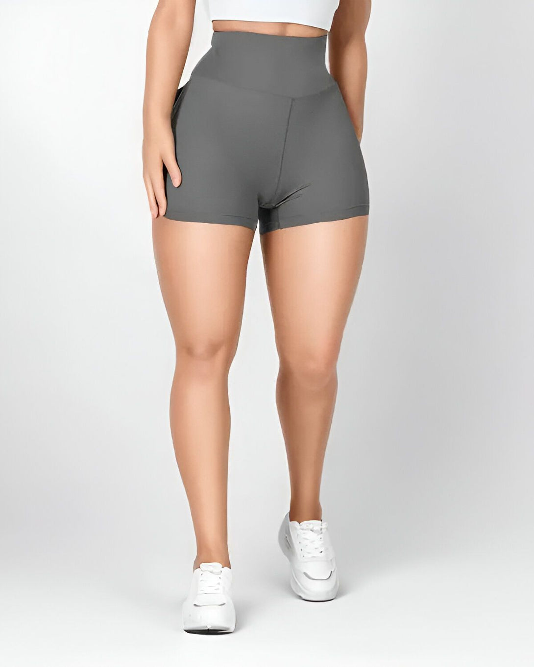 Une femme porte un short moulant gris taille haute avec des baskets blanches.