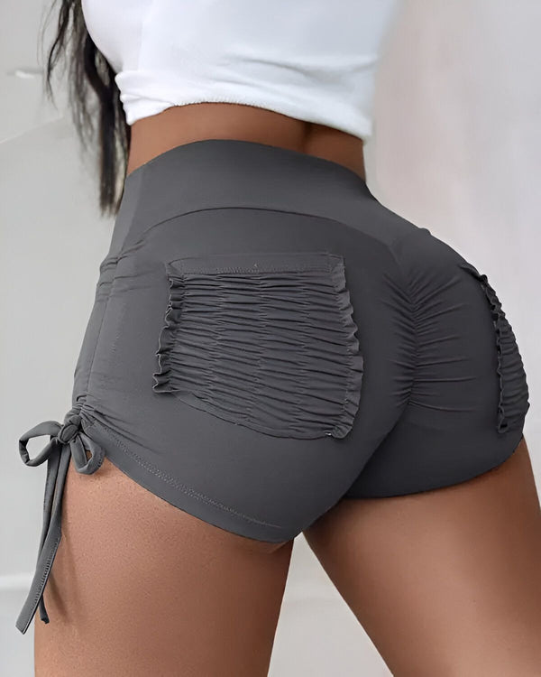 Une femme porte un short de sport gris moulant avec des poches et des cordons de serrage à la taille.