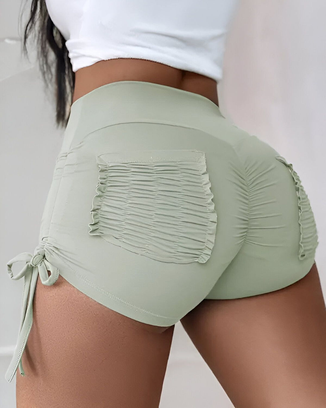 Une femme porte un short moulant vert olive avec des détails froncés au dos.