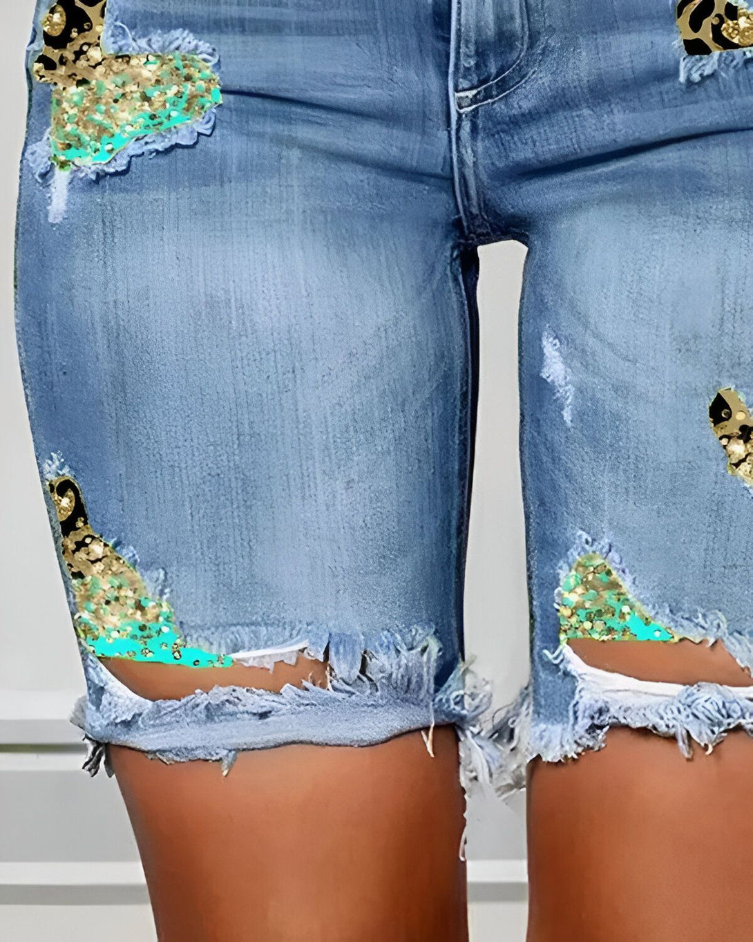 Le mannequin porte un short en jean bleu déchiré avec des sequins turquoise et des motifs léopard dorés.