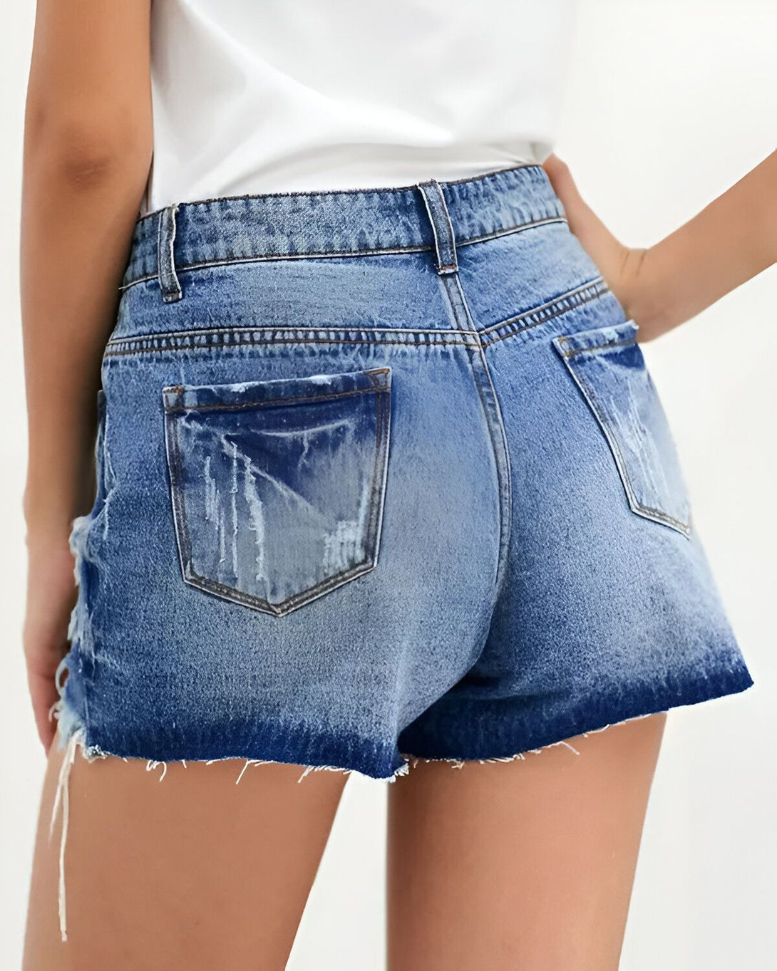 Une femme porte un short en jean bleu déchiré taille haute avec des poches à l'arrière.