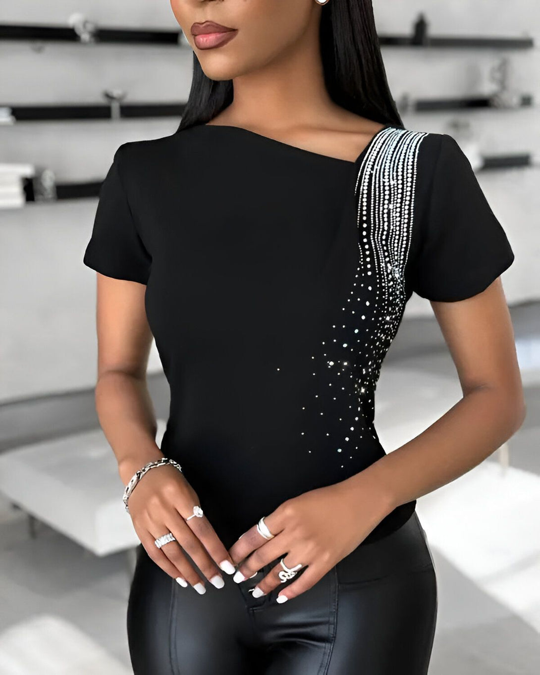 Une femme porte un chemisier noir à manches courtes avec des strass sur l'épaule.